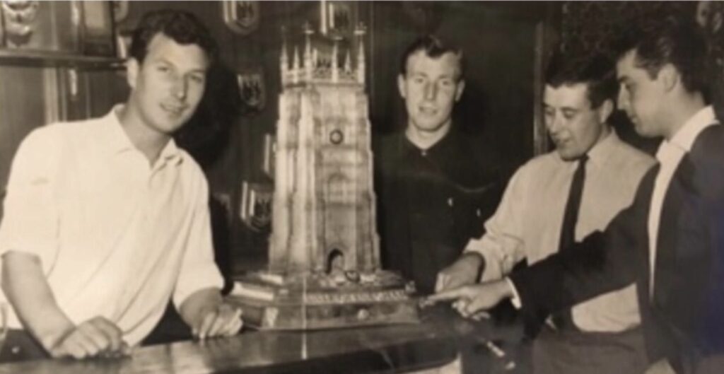 Four men stand around a trophy in the shape of a bell tower.
